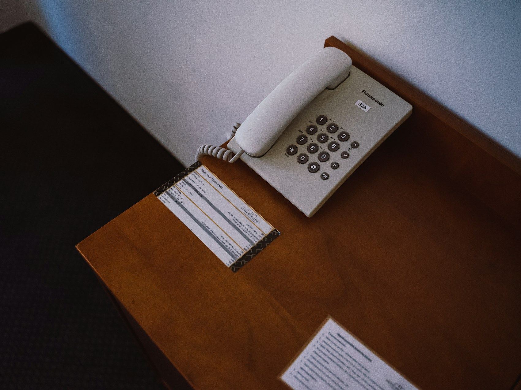 A white corded telephone sits on a wooden desk with a notepad nearby.