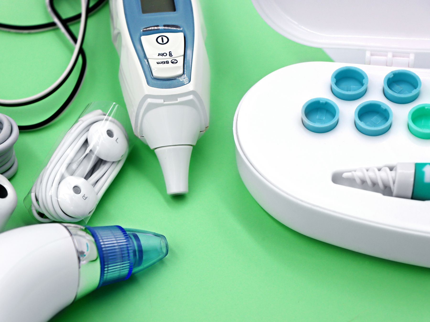 Various ear care devices, ear buds, and cleaning tools laid out on a green surface.